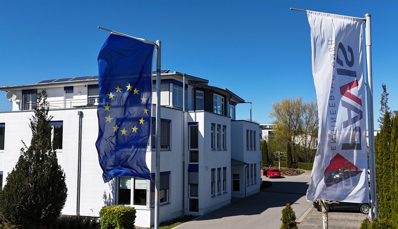 Pavis Gebäude; EU-Flagge und Banner wehen davor; blauer Himmel, roter Wagen im Hintergrund.
